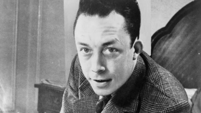 Retrato em preto e branco do escritor francês Albert Camus, de sobretudo, com cigarro
