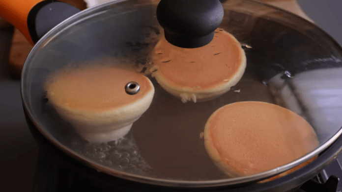 Frigideira tampada com as panquecas dourando do outro lado
