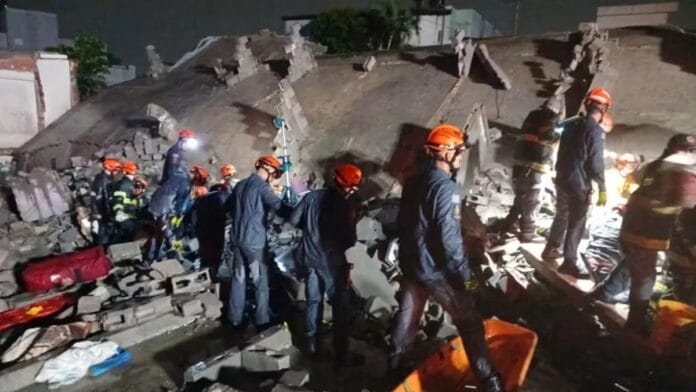 Escombros de um prédio de 12 andares sobre a rua, com bombeiros no local procurando vítimas