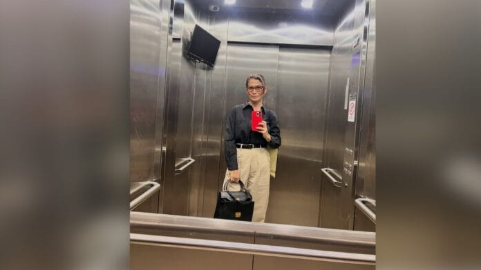 Jornalista Renata Vasconcellos, de cabelo castanho e óculos de armação escura, com blusa preta e calça bege
