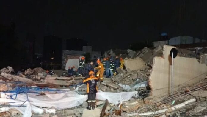 Escombros de um prédio de 12 andares sobre a rua, com bombeiros no local procurando vítimas