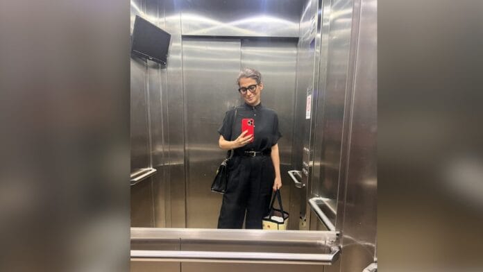 Jornalista Renata Vasconcellos, de cabelo castanho e óculos de armação escura, com blusa de manga curta e calça de alfaiataria em preto