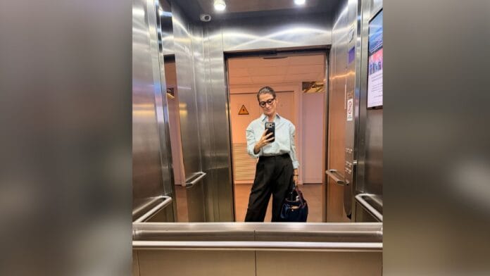 Jornalista Renata Vasconcellos, de cabelo castanho e óculos de armação escura, com blusa branca e calça de alfaiataria em preto