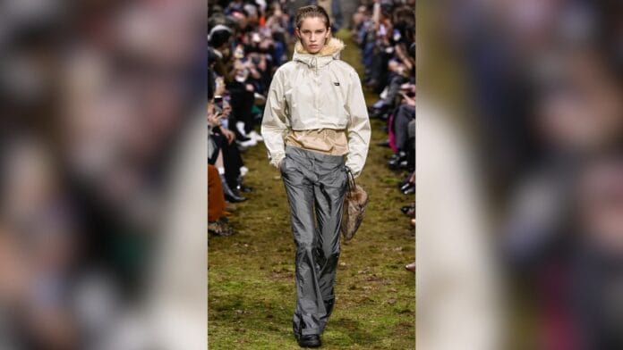 Mulher com calça de nylon cintura baixa cinza, com blusa bege por baixo e uma jaqueta cropped gola alta