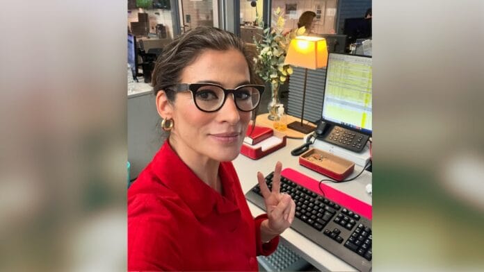 Jornalista Renata Vasconcellos, de cabelo castanho e óculos de armação escura, com camisa social vermelha e brincos dourados