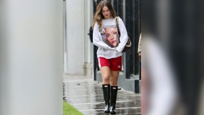 Mulher com blusa de manga comprida branca estampada, short vermelho da marca adidas e bota preta de cano longo