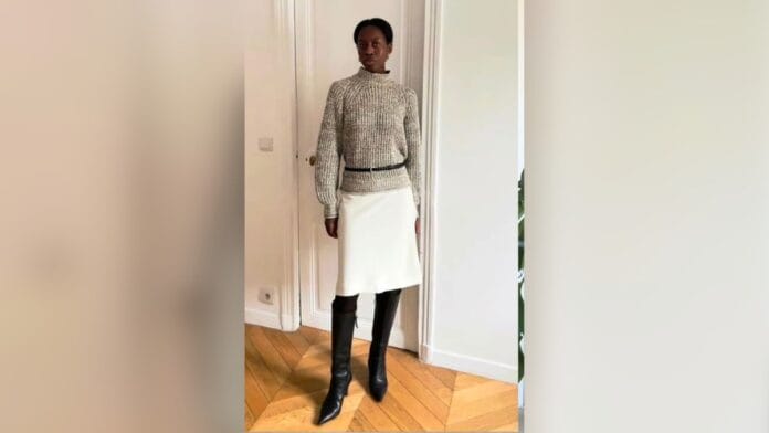 Mulher com saia lápis branca, suéter cinza claro e cinto, com bota preta cano longo