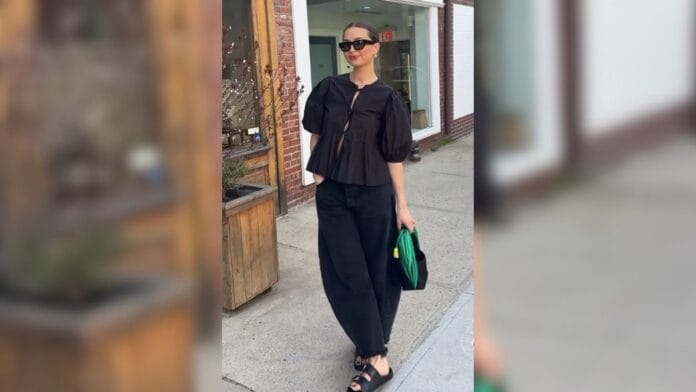 mulher com bata preta, calça de alfaiataria preta, sandália preta e óculos escuros
