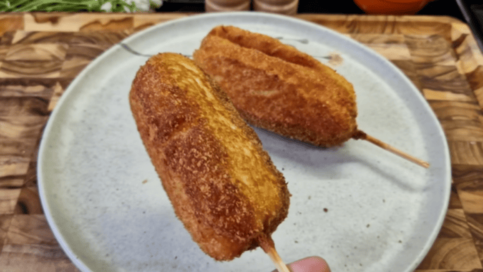 Dois hot dogs coreanos fritos e dourados servidos no palito sobre um prato