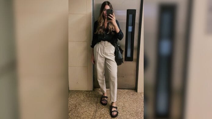 mulher com calça de alfaiataria bege, blusa preta e papete preta