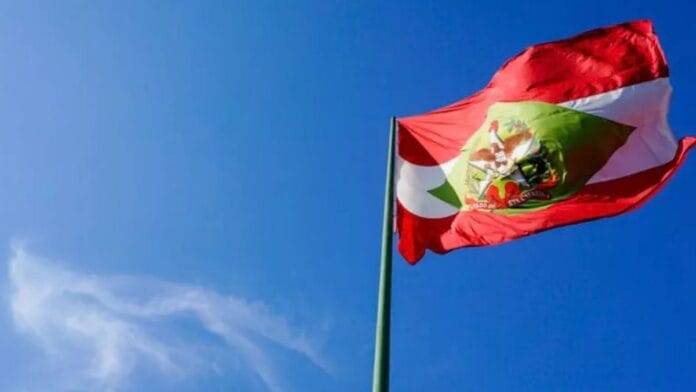 Bandeira do Estado de Santa Catarina a ondular num mastro sob céu azul, representativa da apuração ao vivo para as vagas de senador nas Eleições 2026.