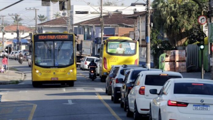 Rua com trânsito intenso, filas de carros e ônibus amarelo