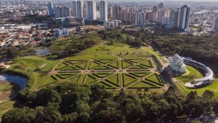Vista aérea dos jardins geométricos do Jardim Botânico com o horizonte de prédios de Curitiba ao fundo, ilustrando a apuração para deputado federal pelo Paraná.