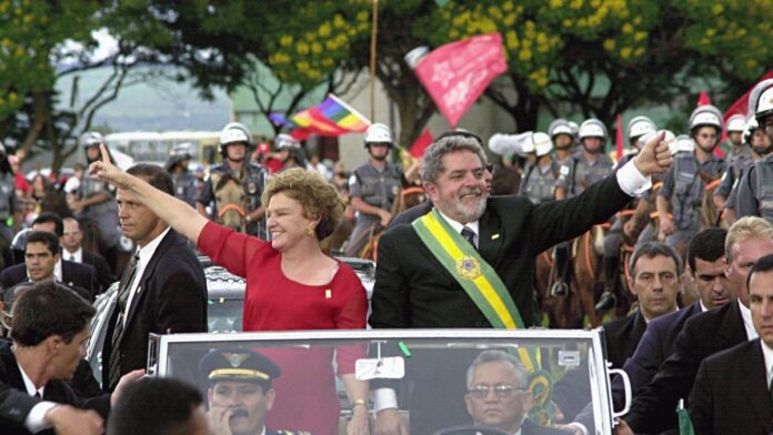 Lula com a faixa presidencial e Marisa Letícia em vestido vermelho desfilam no Rolls-Royce cercados por seguranças e apoiadores.