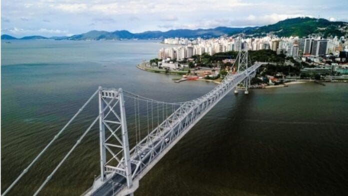 Vista aérea da Ponte Hercílio Luz e da orla de Florianópolis, ilustrando a apuração ao vivo para as 16 vagas de deputado federal por Santa Catarina.