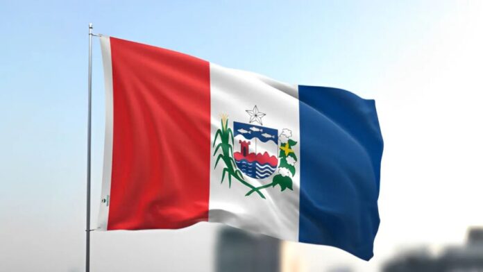 Bandeira do estado de Alagoas com faixas verticais em vermelho, branco e azul e o brasão ao centro, hasteada e ondulando, ilustrando a apuração geral das Eleições 2026