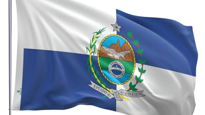 Bandeira do Estado do Rio de Janeiro hasteada, com as suas cores azul e branca e o brasão ao centro, representando a apuração geral das Eleições 2026.