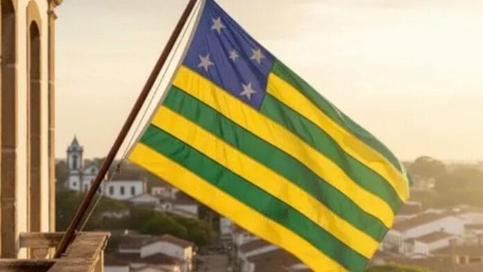Bandeira do Estado de Goiás com listras horizontais verdes e amarelas e cantão azul com estrelas brancas, hasteada e ondulando, representando a apuração geral das Eleições 2026
