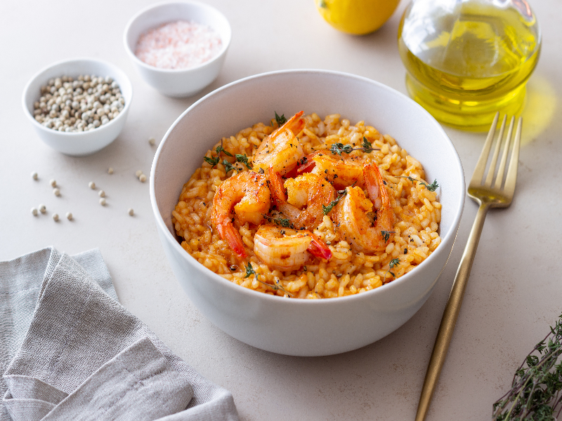 Arroz de camarão com leite de coco Recipiente branco com arroz cremoso vermelho e camarões em cima