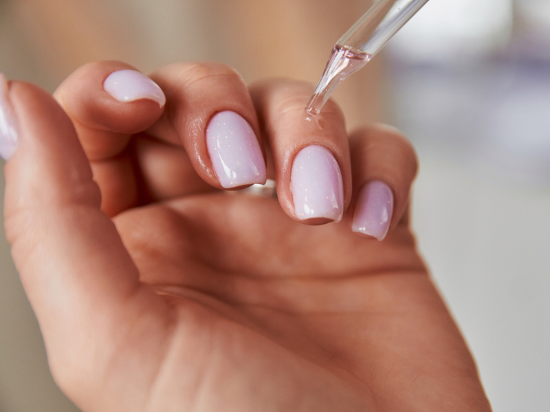 Unhas pintadas de rosa bebê e cutículas sendo hidratadas com óleo
