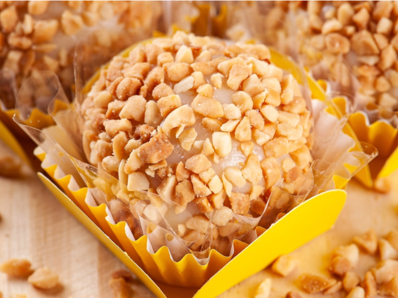 Brigadeiro de amendoim Brigadeiro decorado com pedaços de amendoim em cima de um papel amarelo